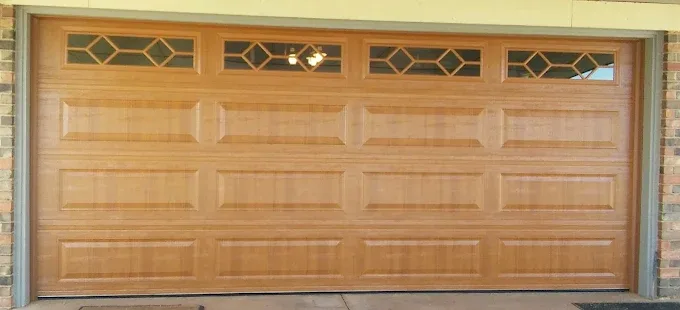 Wood-look garage door with diamond windows on brick home by Affordable Door Co OKC